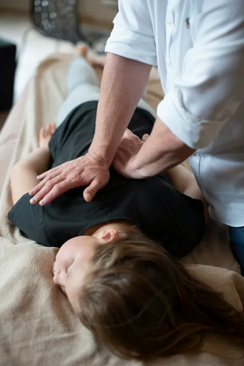 Therapeut drückt mit beiden Händen auf den Rücken einer bekleideten Patientin